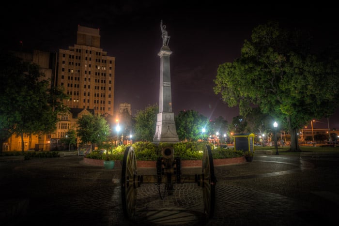 Una foto de una estatua y un canon en una plaza, que se encuentra en el embrujado San Antonio, Texas.